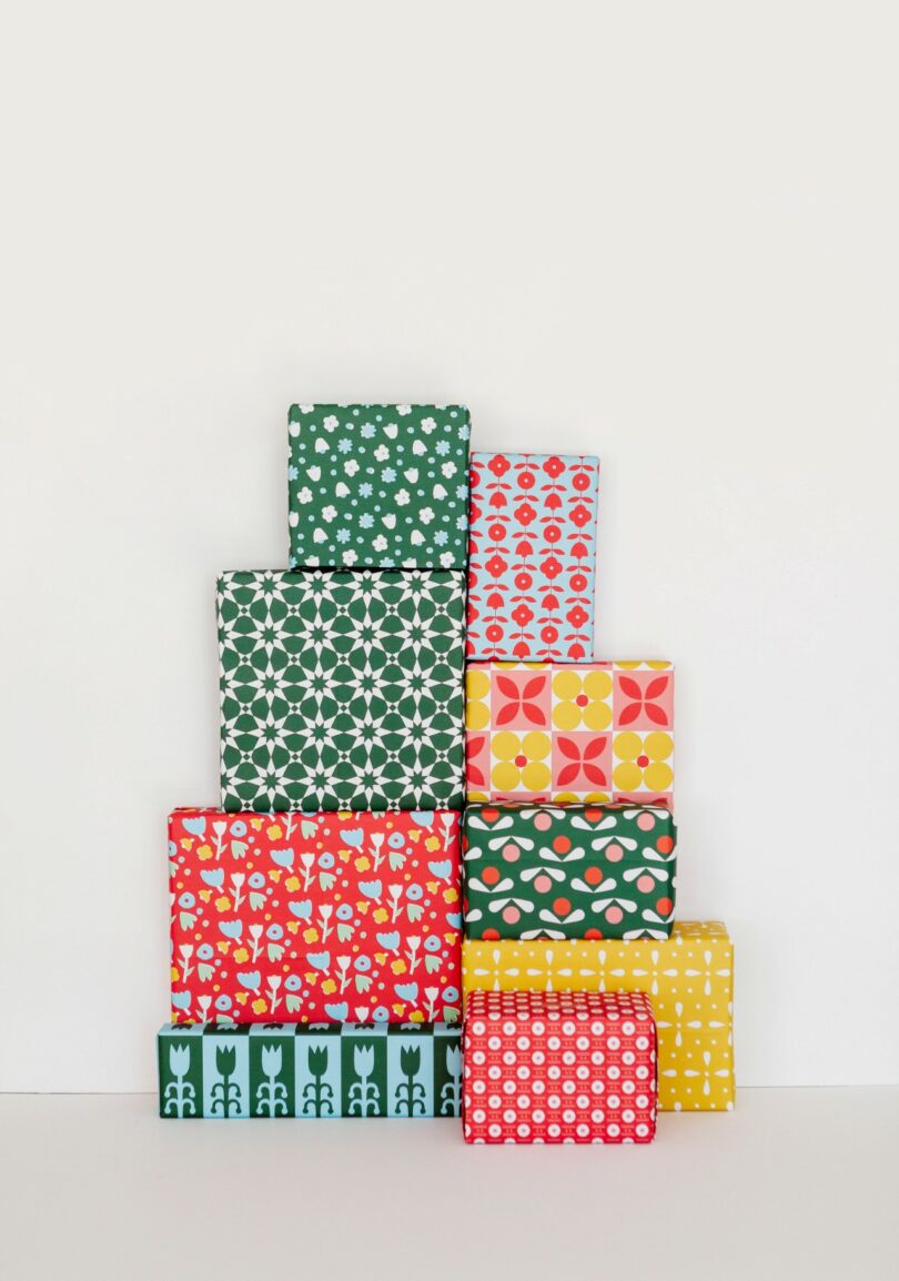 A stack of nine gift boxes wrapped in colorful patterned paper, arranged in a pyramid against a plain white background, reminiscent of Amanda Jane Jones’ signature modern style