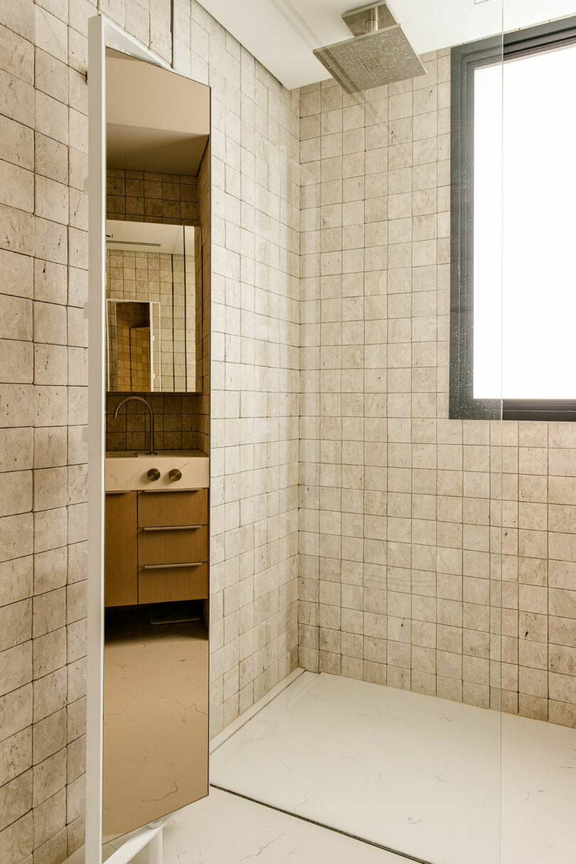 Modern bathroom with beige square tile walls, a walk-in shower with a ceiling-mounted showerhead, a rectangular mirror, a floating vanity, and a large window providing natural light.