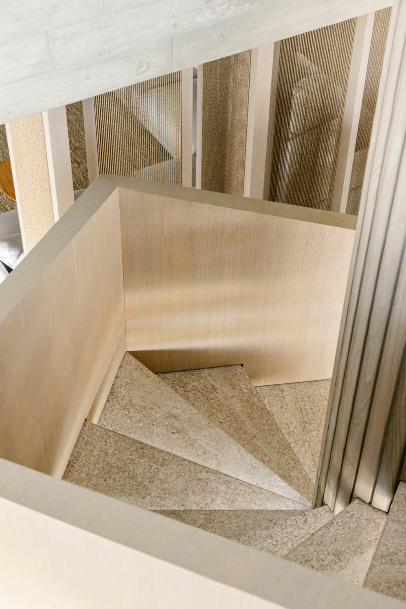 A top-down view of a modern, light wood spiral staircase with textured steps and vertical slatted railing.
