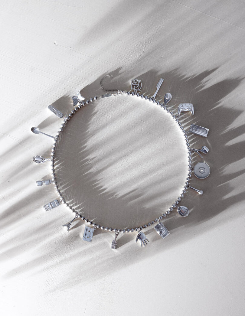 A circular bracelet with multiple small charms casts shadows on a light-colored surface.