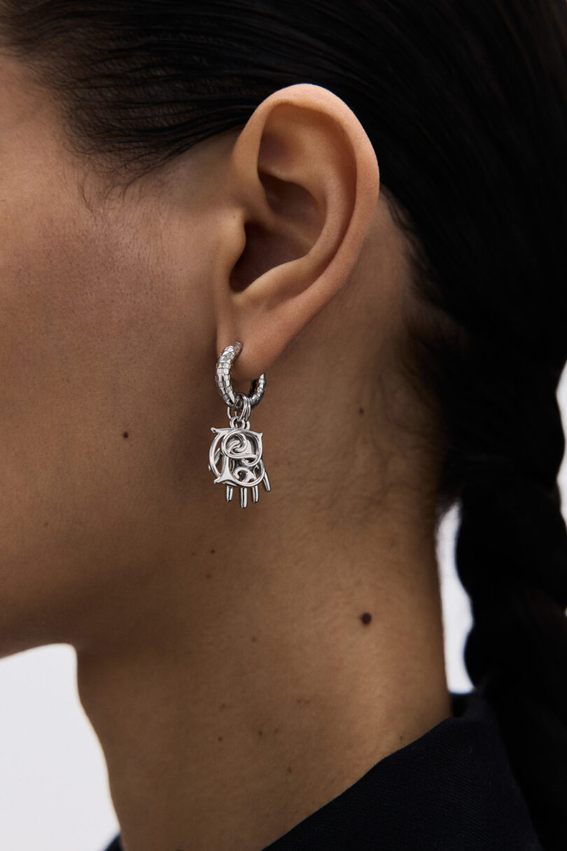 Close-up of a person's ear wearing a silver, ornate earring with a geometric and claw-like design; hair is dark and braided.
