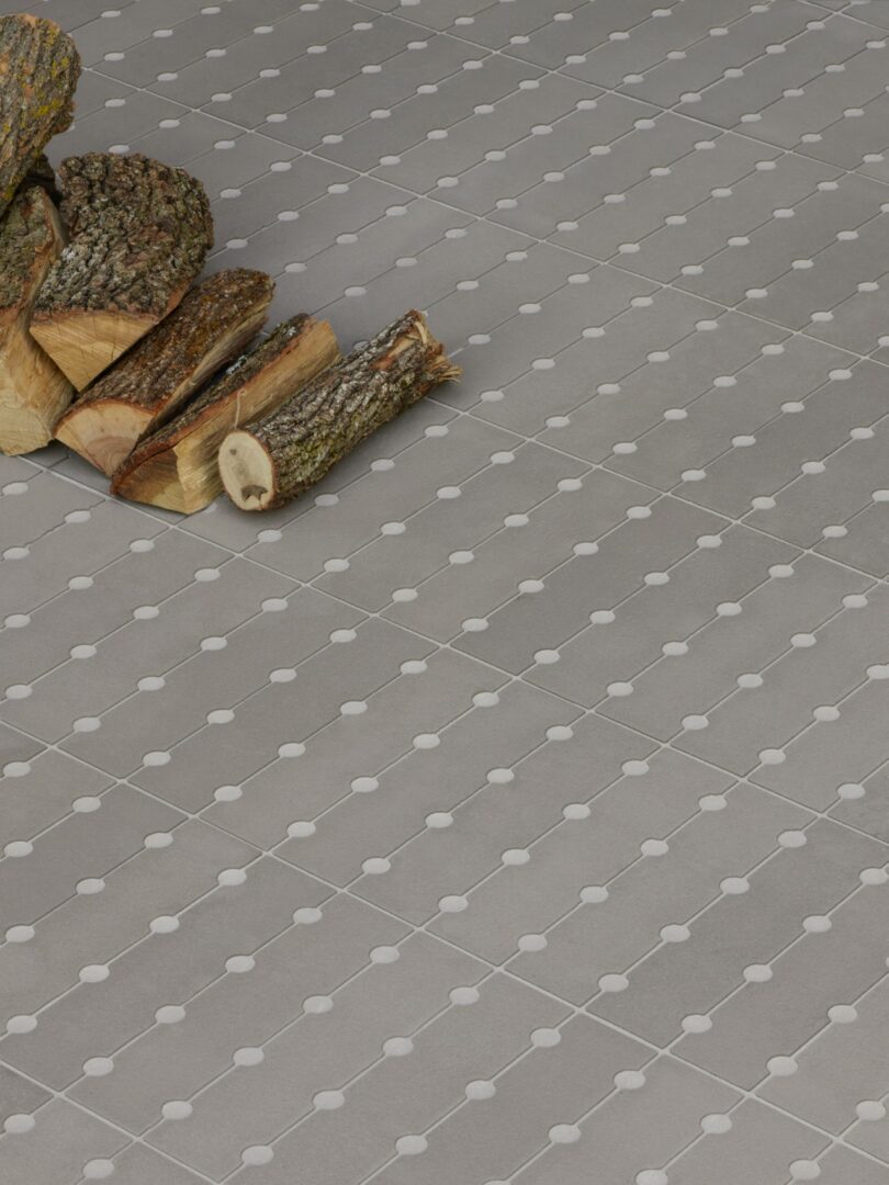 A small stack of firewood sits on a gray tiled floor with a geometric pattern of dots and lines