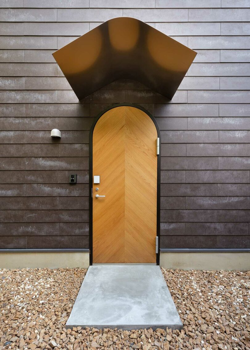 angled view of modern home exterior with dark siding and light wood front door