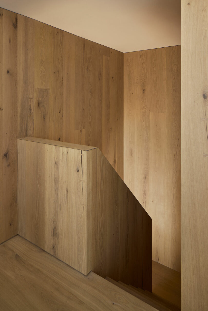Minimalist wooden staircase with light brown wood paneling on walls and banister, and soft lighting highlighting the clean, modern design.