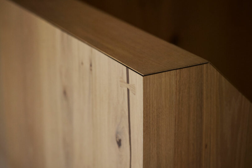 Close-up of a wooden surface with a visible dovetail joint and natural wood grain, showing precise craftsmanship and a smooth angled edge.