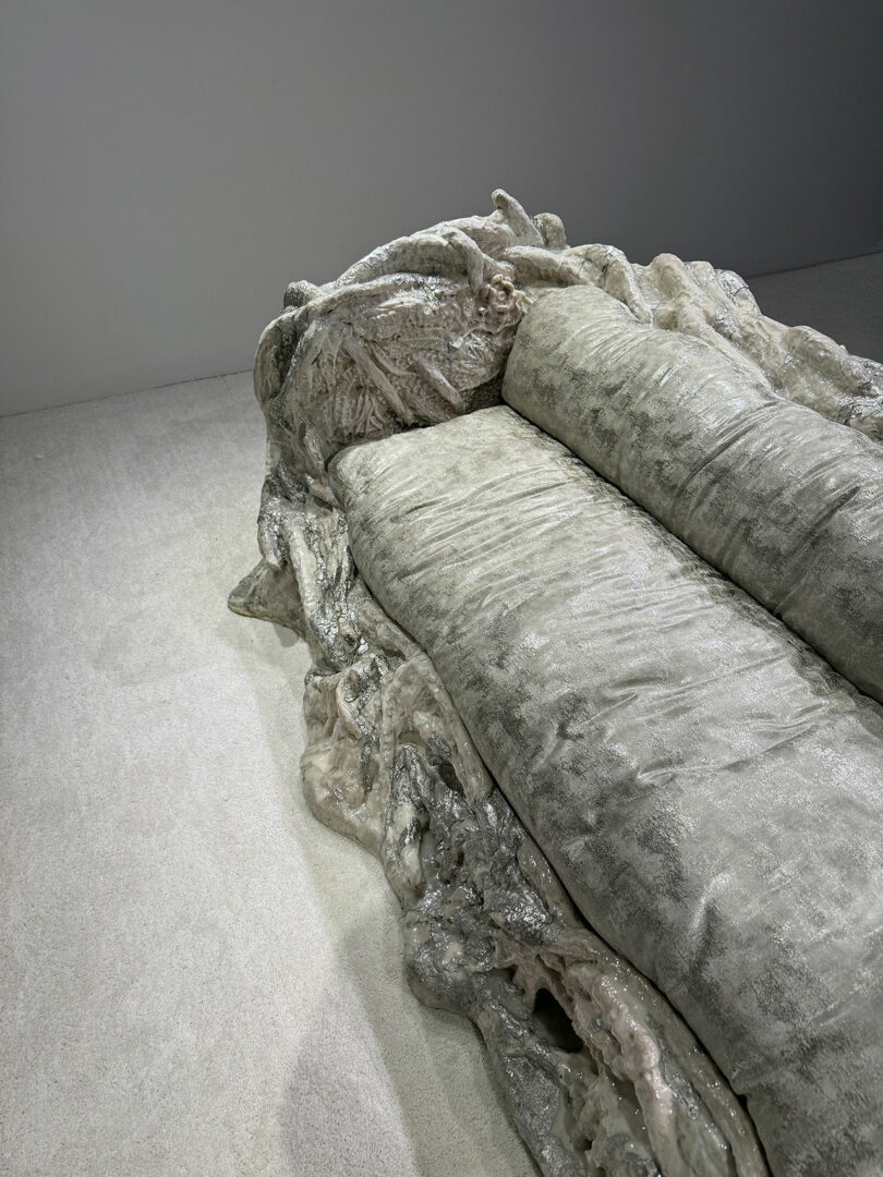 A sculptural, metallic-textured couch with an organic, rock-like base sits on a light-colored carpet against a plain wall.