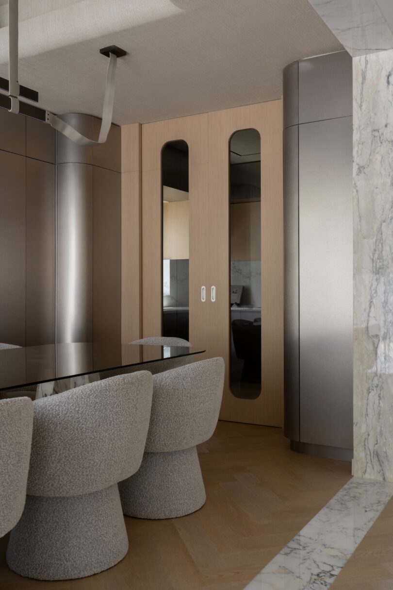 Modern dining area with textured gray chairs, a glossy black table, wood and metallic wall panels, and marble flooring accents.