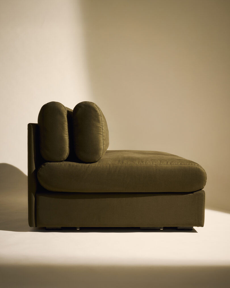A minimalist olive green chaise lounge with two back cushions, set against a plain background with soft lighting.