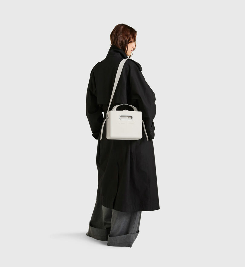 Person wearing a long black coat and wide-leg gray pants, carrying the PARSEL EVA Tote System over the shoulder, stands against a plain white background.