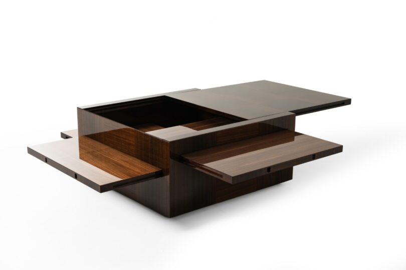 Modern wooden coffee table with a cube design featuring multiple sliding panels revealing hidden storage compartments, set against a white background