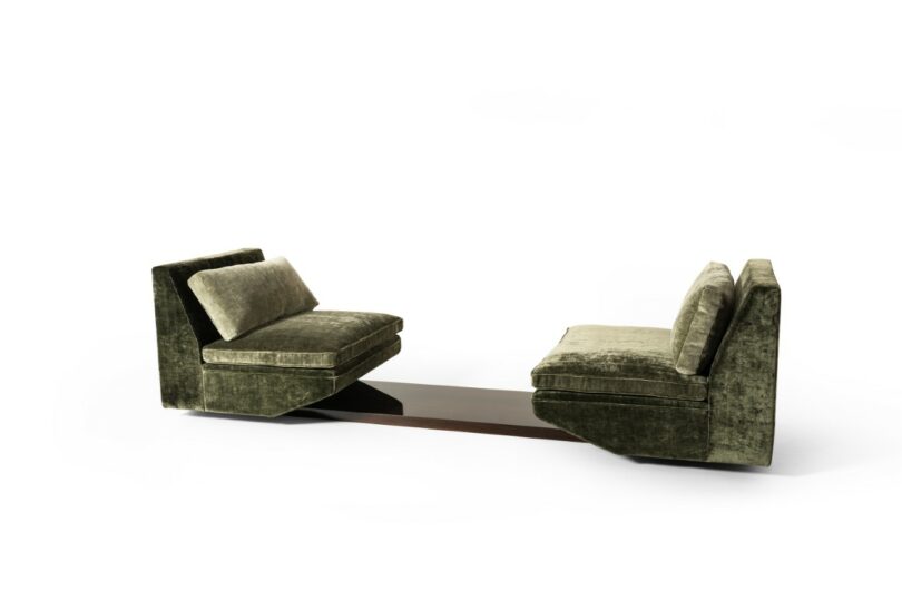 Two green velvet armchairs facing each other, connected by a low, dark wooden table between their bases, against a plain white background