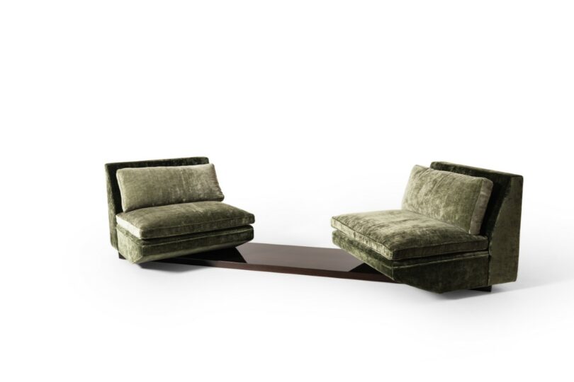 Two green velvet armchairs next to each other, connected by a low, dark wooden table between their bases, against a plain white background
