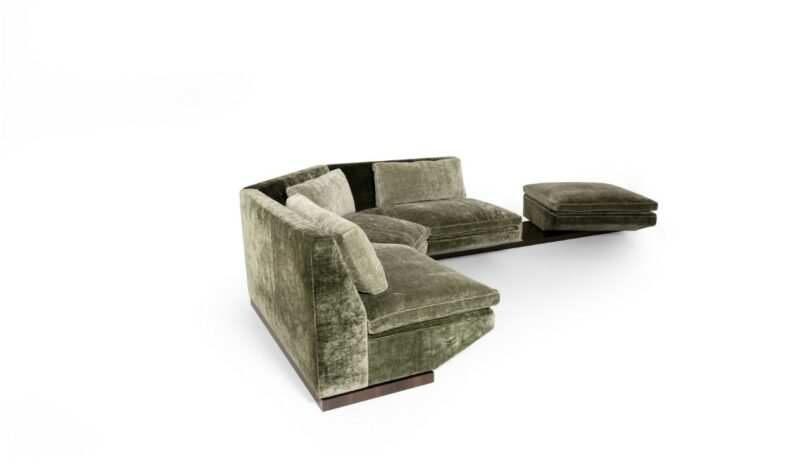 Green velvet sectional sofa with three seats, an attached wooden side table, and a matching ottoman, all set against a white background.