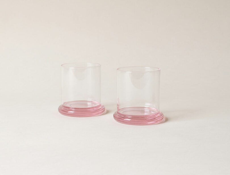 Two clear glass tumblers with pink bases are placed side by side on a neutral background.
