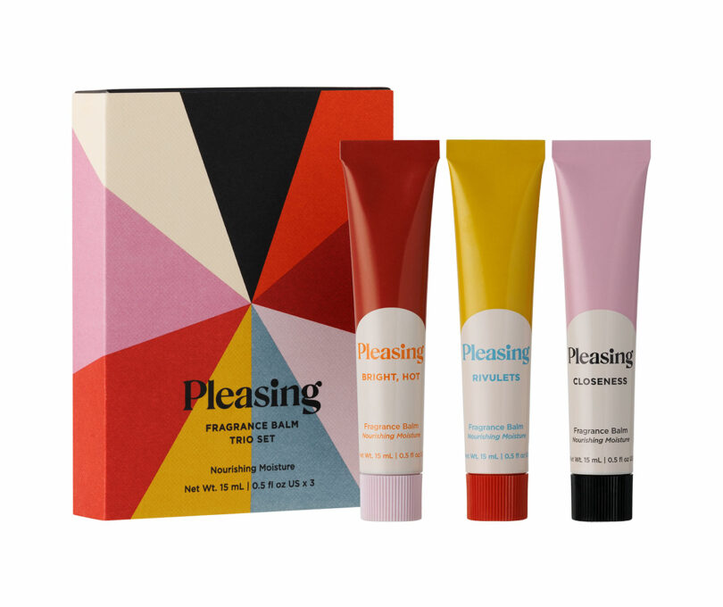 Three tubes of Pleasing fragrance balm (red, yellow, pink) stand beside a colorful geometric box labeled "Pleasing Fragrance Balm Trio Set.