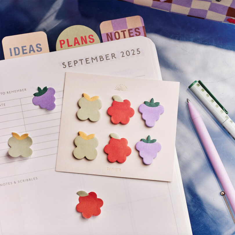 A planner open to September 2025 with labeled tabs, fruit-shaped sticky notes, a pen, and a clear ruler arranged on a desk.