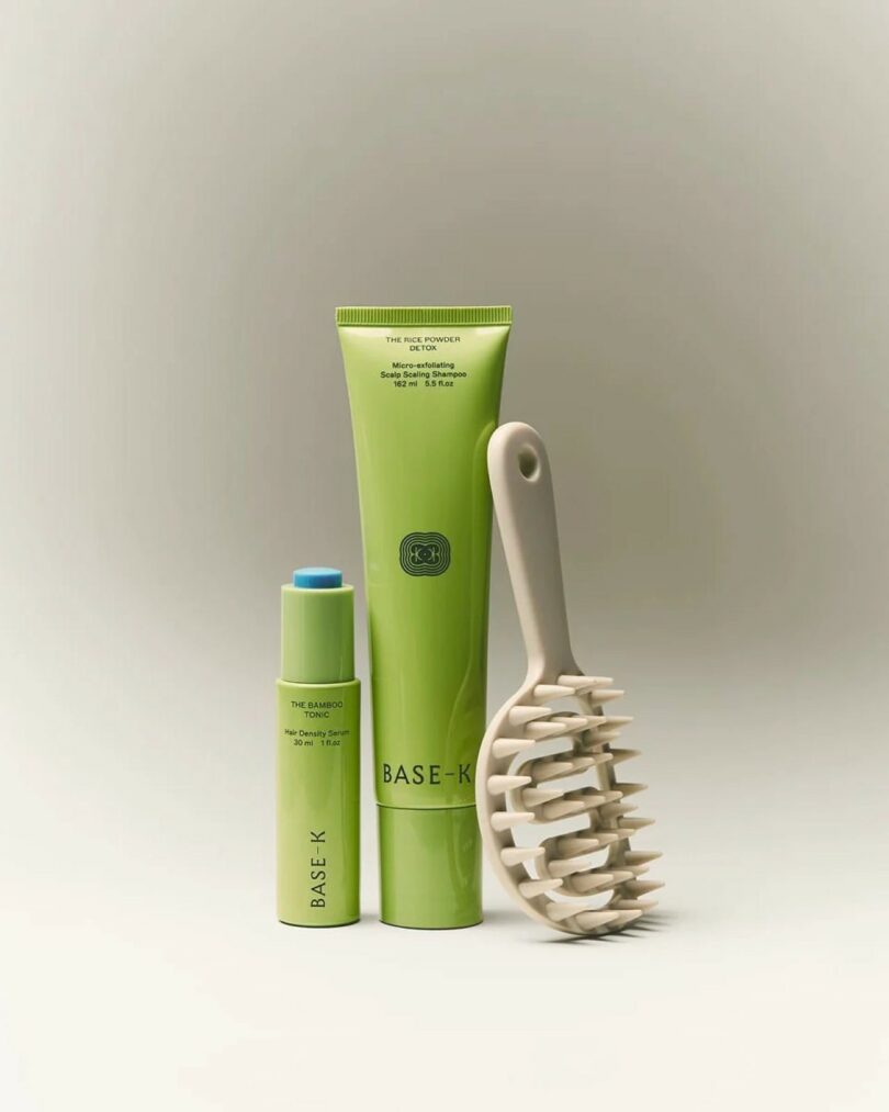 Three personal care items: two green tubes labeled "BASE-K" and one light-colored scalp massager with rounded bristles, arranged on a neutral background