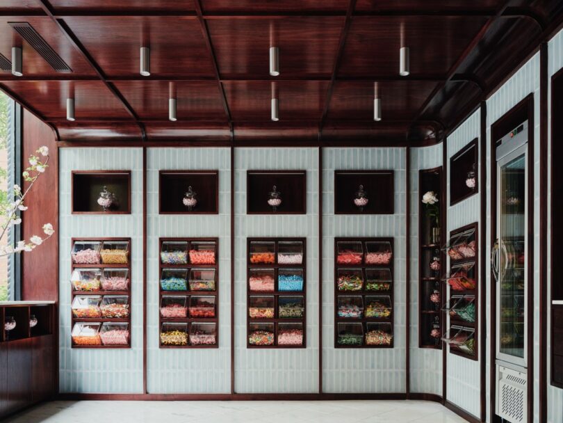 A modern candy shop interior with wooden shelves filled with colorful candies in clear bins, tiled walls, and pendant lights hanging from the ceiling