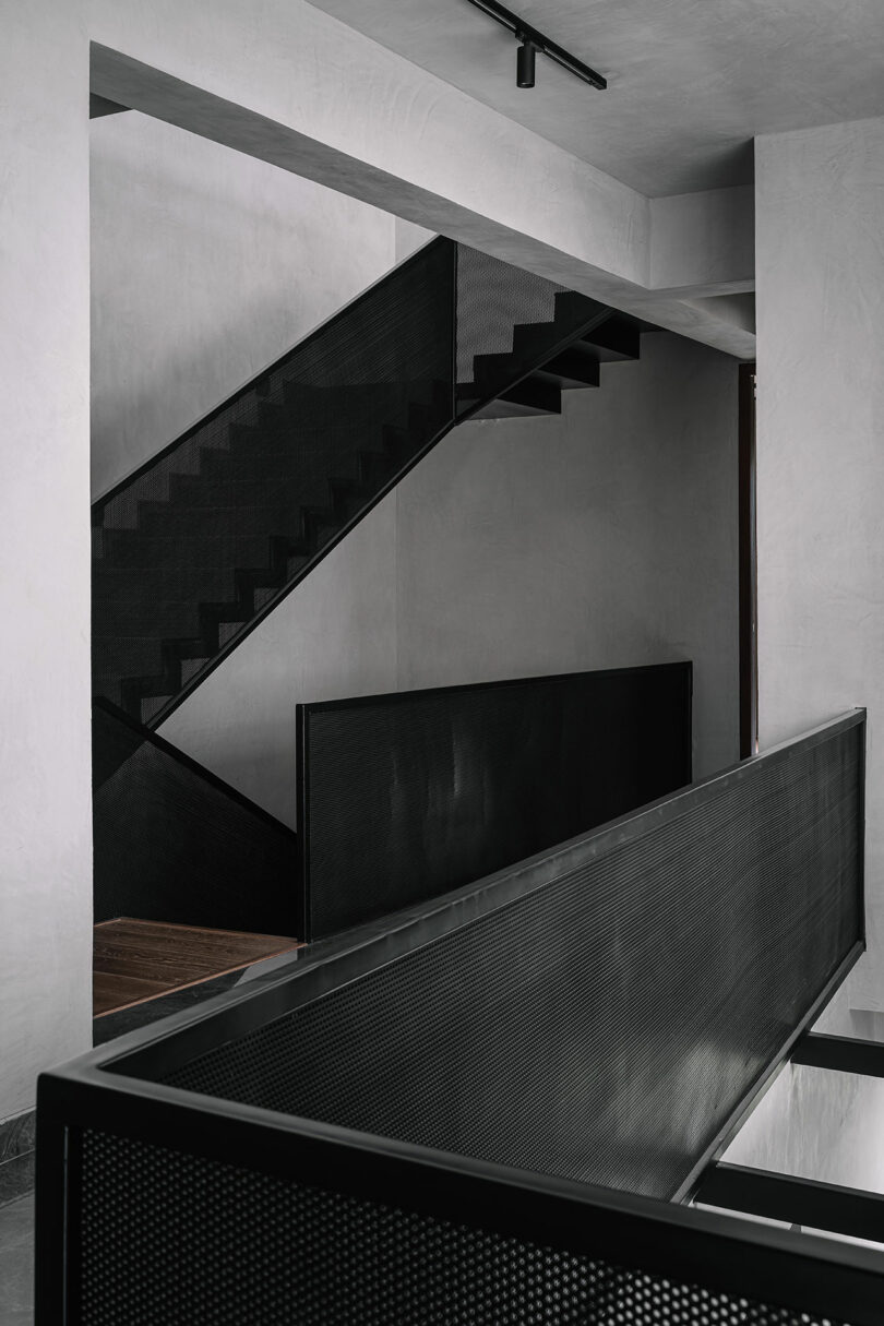 Minimalist interior featuring black metal staircases, mesh railings, and concrete walls in a modern architectural design.