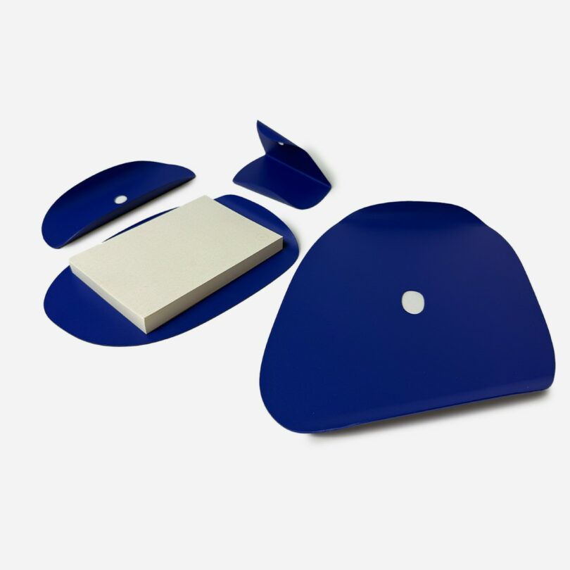 A white notepad with dotted pages sits among several flat, irregularly shaped blue objects on a white surface