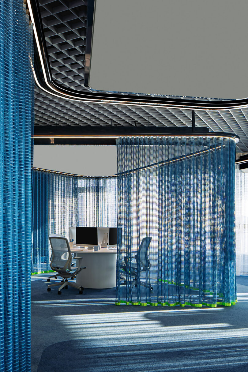 Modern office space with curved workstations, ergonomic chairs, and blue mesh curtains creating semi-private areas under a geometric ceiling.