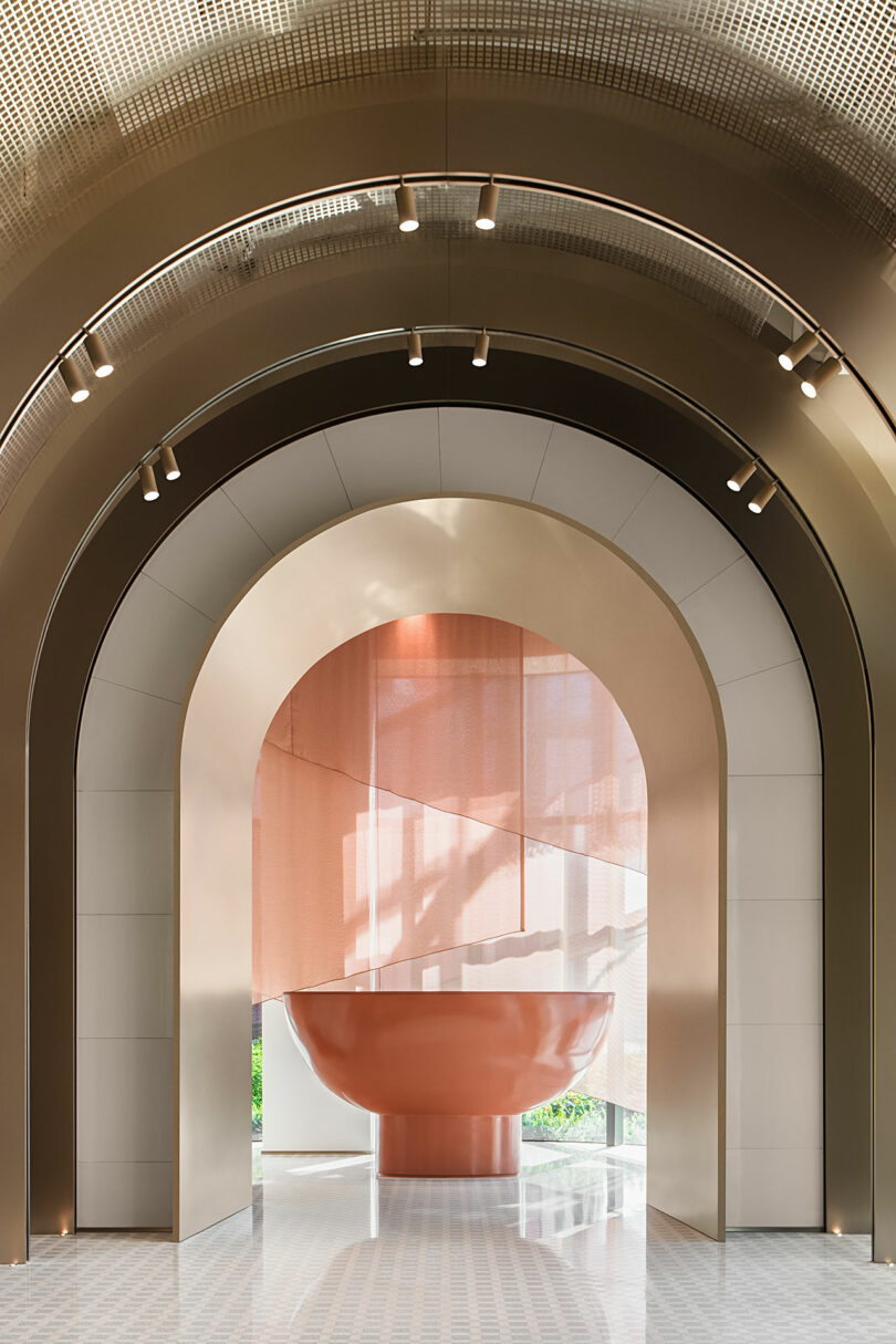 Modern interior with multiple metallic archways, recessed lighting, and a large sculptural copper bowl in the center, with natural light filtering through sheer pink curtains.