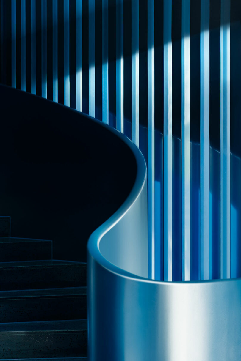 Curved blue staircase with vertical blue and white light bars beside it, creating a modern, abstract architectural scene.