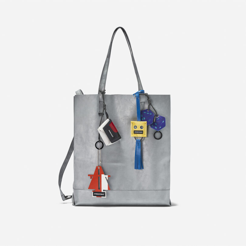 A metallic silver tote bag with four colorful keychain charms attached to the handles, displayed against a plain white background.