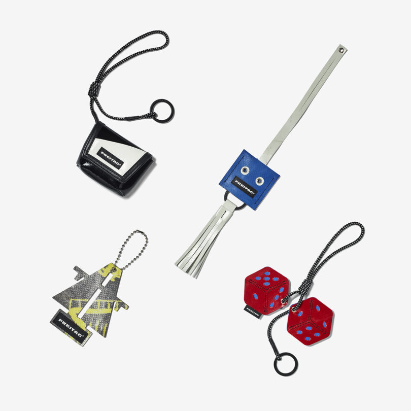 Four designer keychains are displayed on a white background: a black purse, a blue robot, a yellow arrow, and a pair of red dice.