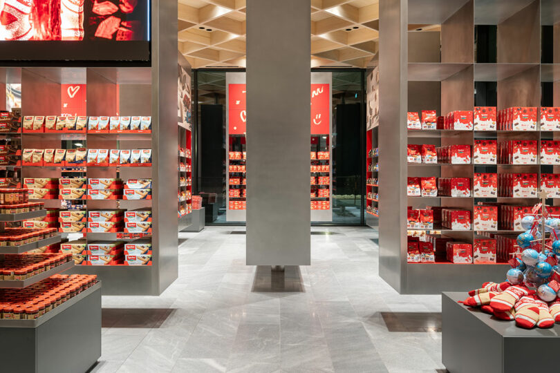 A modern retail store interior with shelves displaying neatly arranged red and white packaged products, gray floors, and metallic shelving units.