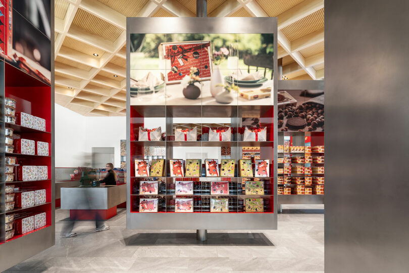 Modern retail store interior with shelves displaying assorted packaged products, including chocolates and gift boxes; cashier counter visible in the background.