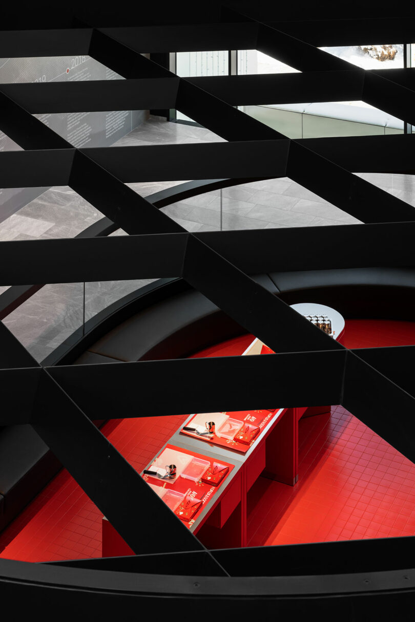 View through a black grid structure onto a red-tiled display area with several exhibited items and informational panels in a modern, well-lit interior space.