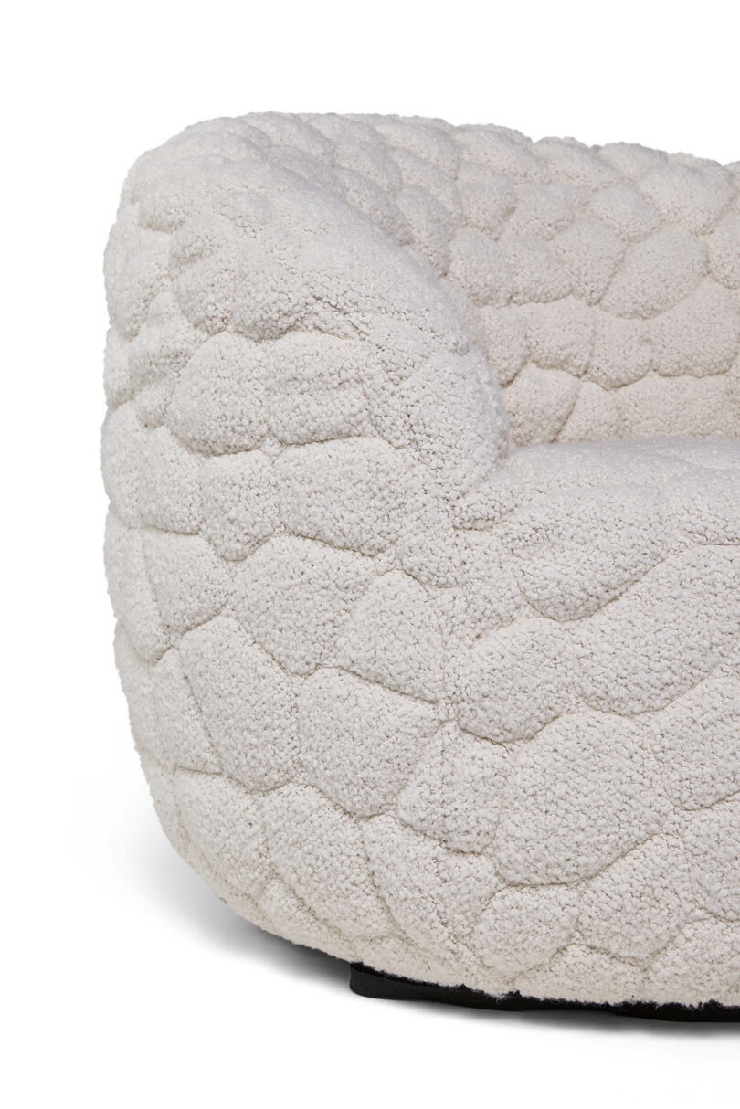 Close-up of a textured, off-white upholstered chair with a hexagonal pattern resembling a quilted or tufted surface.