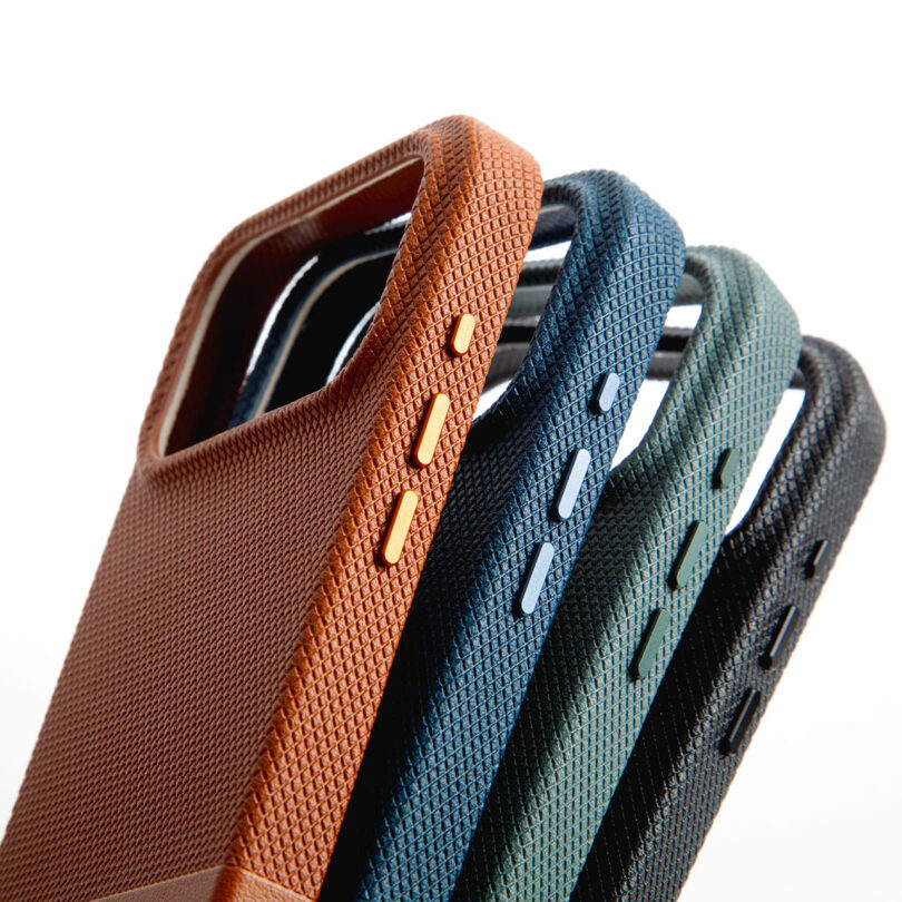 Four textured phone cases in brown, blue, green, and black are stacked at an angle, showing side buttons and rear camera cutouts against a white background.