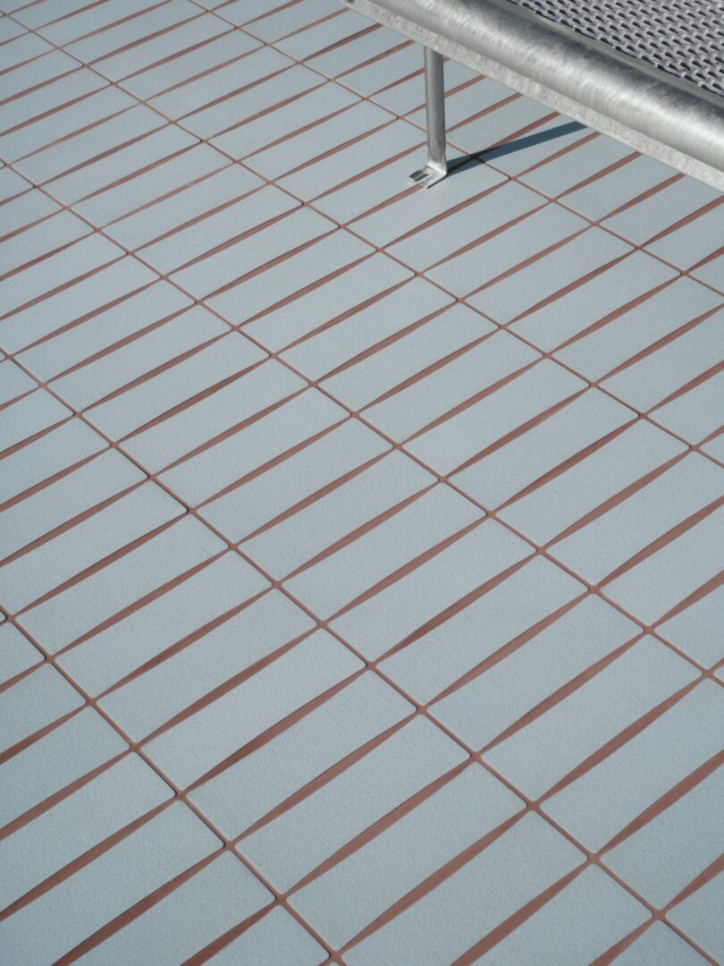 A metal bench is positioned on a tiled floor with a grid pattern of light blue tiles and brown grout lines