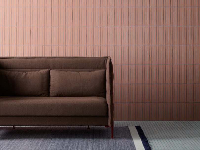 A brown sofa with two cushions is positioned on a blue and white rug against a pink wall with vertical blue stripes