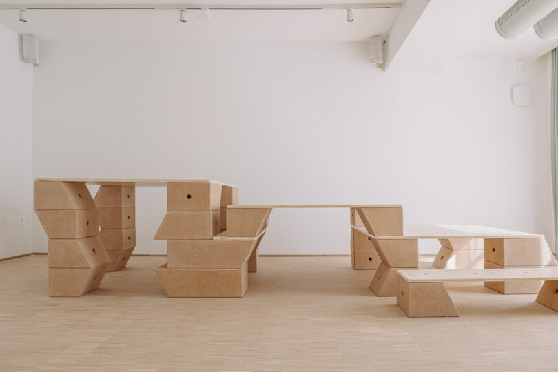 Minimalist room with modular wooden furniture, including a table, bench, and seating, set on a light wood floor against a white wall