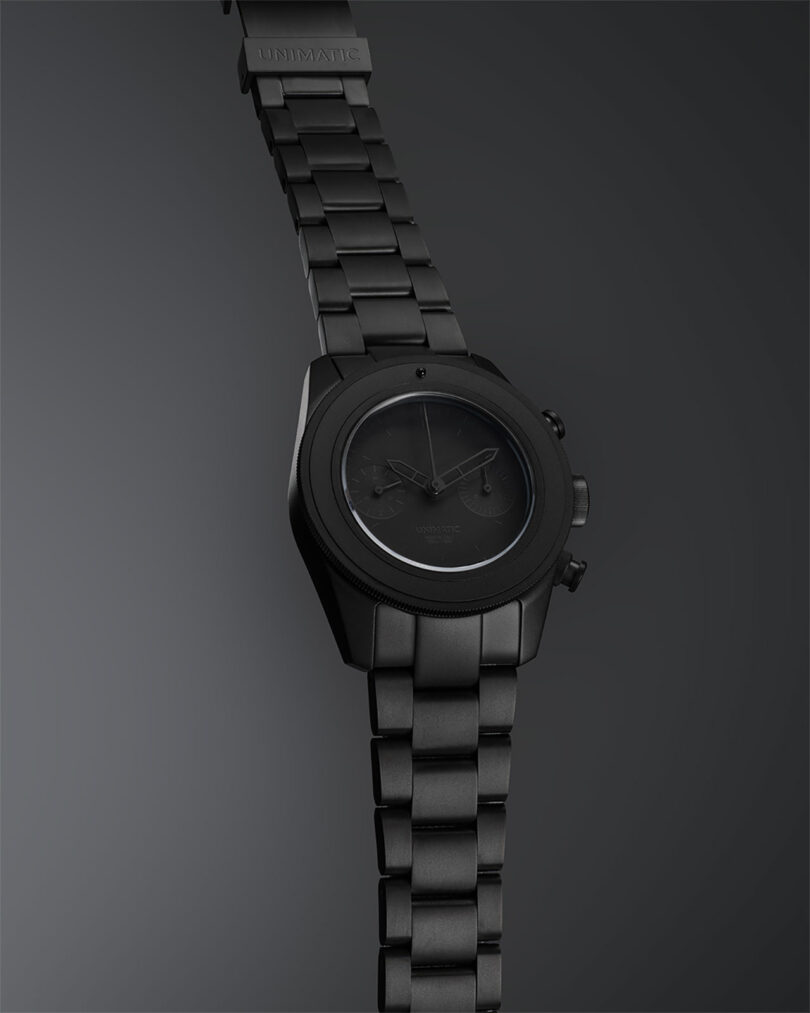 A matte black wristwatch with a metal link band and minimalist design on a dark gradient background.