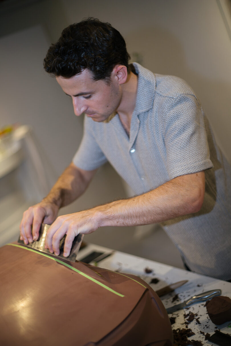 A person in a short-sleeved shirt grates chocolate over a large chocolate dome on a countertop.