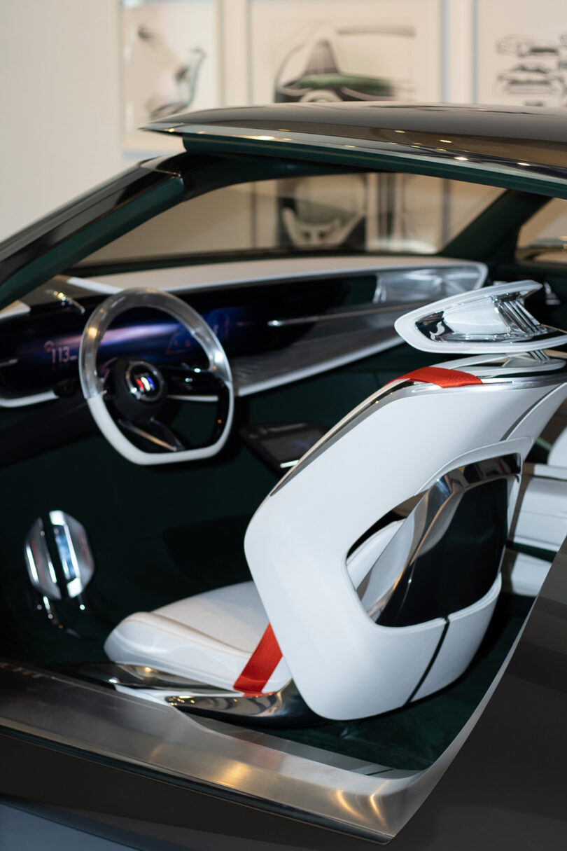 Futuristic car interior with a white and red driver's seat, digital dashboard, and modern steering wheel, shown from the passenger side.